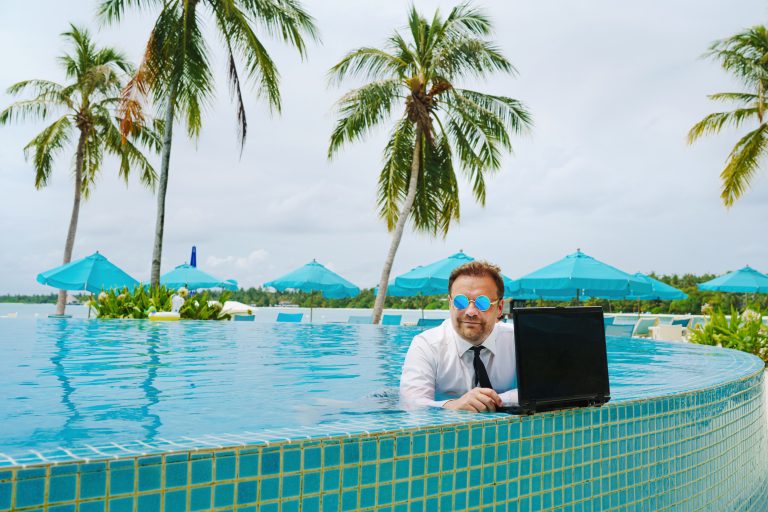 Mann im Anzug steht mit Laptop im Pool